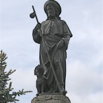  St Roch, patron des pèlerins sous le double aspect du pèlerin au large chapeau avec la coquille et du pestiféré secouru par un chien, découvrant son genou pour montrer sa plaie. 