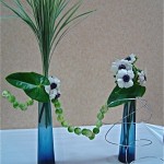 Des choux de Bruxelles enfilés sur du fil à bonsaï animent le duo de bouteilles bleues. Atelier Inspirations Florales.