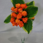 Bouquet de roses oranges et hostas panachés de blanc dans une flûte en verre.