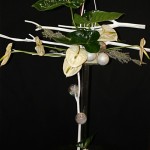 Sur un support transparent, quelques branches de Mitsumata blanchies garnies de fleurs et feuilles d'Anthuriums