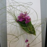 Sur un châssis entoilé, le bouquet d'orchidées Vanda est souligné par un jeu de volutes végétales.