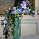 Une gerbe de fleurs variées est disposée sur le vase : lysianthus, hortensias, aconit. 