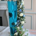 Une élégante guirlande de fleurs fraîches descend le long du vase en verre rempli d'eau colorée.