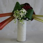 Décor de jardin sur un cylindre blanc avec rhubarbe et oeillets de poète rouge à l'arrière du bouquet.