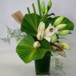 Dans un vase en verre,les lys blancs accompagnent les palmes.