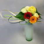 Bouquet rond multicolore  sur un haut vase cylindre en verre coloré.